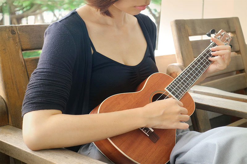 Girl playing a Tenor ukulele while sitting down outside