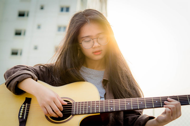 Female guitarist playing acoustic guitar with sun setting in the background